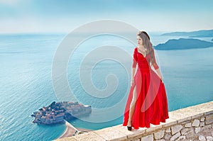 Beautiful Fashion Girl model in gorgeous red dress over the sea, blue sky. Sveti Stefan, Montenegro. Freedom concept. Travel. Vac photo