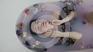 Beautiful fashion model girl in milk bath with fragrant flowers of buds, touching face skin. Spa and skin care concept