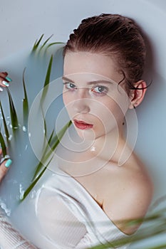 Beautiful fashion model girl taking a milk bath with flowers, advertisement of a skincare product.
