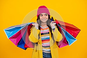 Beautiful fashion teenager child girl with shopping bags on yellow background. Autumn shopping sale. Kid with shopping