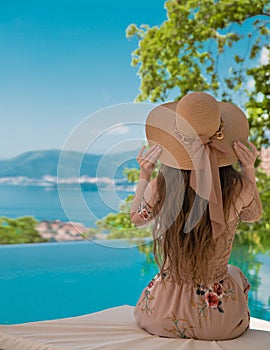 Beautiful Fashion Woman in beach hat enjoying sea view by swimming pool on luxury tropical resort. Exotic Paradise.