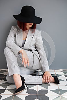 Beautiful fashion woman. Full length portrait of beautiful girl wearing gray suit and black hat sitiing on the floor