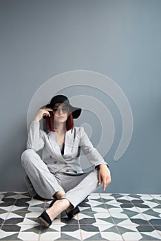 Beautiful fashion woman. Full length portrait of beautiful girl wearing light gray suit and black hat posing indoor