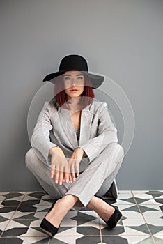 Beautiful fashion woman. Full length portrait of beautiful girl wearing light gray suit and black hat posing indoor over deep