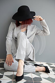 Beautiful fashion woman. Full length portrait of beautiful girl wearing light gray suit and black hat posing indoor over deep