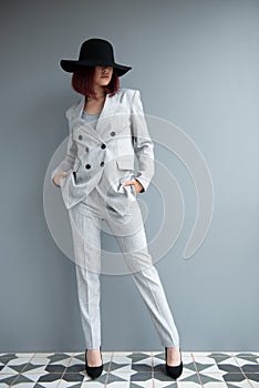 Beautiful fashion woman. Full length portrait of beautiful girl wearing light gray suit and black hat posing indoor over deep