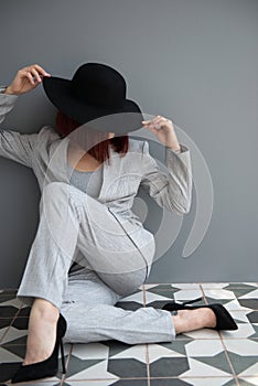 Beautiful fashion woman. Full length portrait of beautiful girl wearing light gray suit and black hat posing indoor over deep