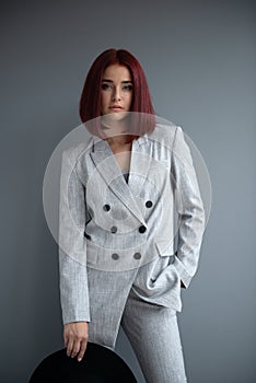 Beautiful fashion woman. Full length portrait of beautiful girl wearing light gray suit and black hat posing indoor over deep