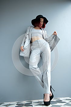 Beautiful fashion woman. Full length portrait of beautiful girl wearing light gray suit and black hat posing indoor over deep