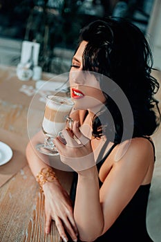 Beautiful fashion woman sitting in street cafe, enjoy aroma taste coffee. Closeup portrait brunette lady with long curls