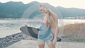 Beautiful and fashion young woman posing with a longboard near sea.