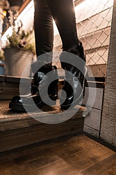 Beautiful fashionable black warm boots close-up. Young trendy woman in winter stylish shoes with fur stands on a wooden staircase