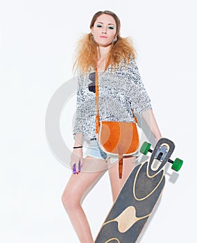Beautiful fashionable blond girl posing with a haughty face with a vintage bag on shoulder holding hand longboard near a white