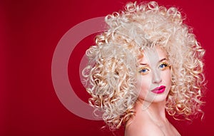 Beautiful fashionable blonde girl in retro style with voluminous curly hairstyle, open shoulders on a red background looks at the