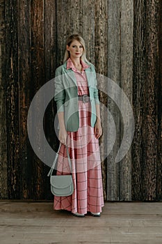 beautiful fashionable blonde girl stands in a pink dress and a mint jacket with a bag in her hands