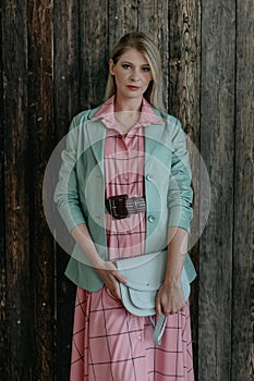 beautiful fashionable blonde girl stands in a pink dress and a mint jacket with a bag in her hands