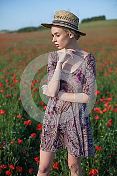 Beautiful fashionable blonde woman in a field of red flowers and a hat with fields