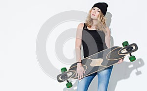 Beautiful fashionable bright young girl in jeans, a black T-shirt and hat posing with a cool longboard in the hands of near a whit