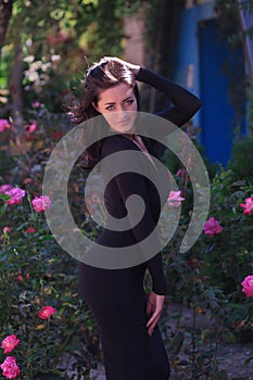 beautiful fashionable brunette woman adult posing in the park on the flowers backgraund in black dress with a cleavage