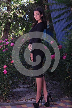 beautiful fashionable brunette woman adult posing in the park on the flowers backgraund in black dress with a cleavage