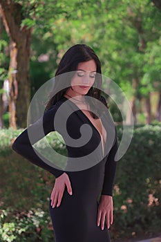 beautiful fashionable brunette woman adult posing in the park on the plants backgraund in black dress with a cleavage