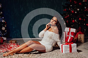 Beautiful fashionable brunette woman at the Christmas tree with gifts for the new year