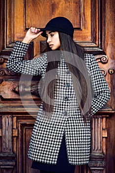 Beautiful fashionable brunette woman with long hair posing near wooden door wearing coat