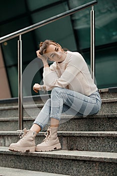 Beautiful fashionable businesswoman sitting on the stairs in front of business center. Outdoor full-length fashion