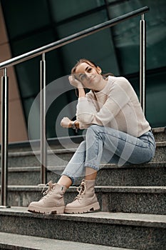 Beautiful fashionable businesswoman sitting on the stairs in front of business center. Outdoor full-length fashion