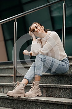 Beautiful fashionable businesswoman sitting on the stairs in front of business center. Outdoor full-length fashion