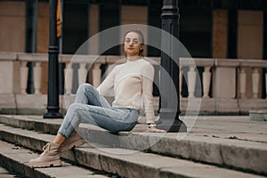 Beautiful fashionable businesswoman sitting on the stairs in front of business center. Outdoor full-length fashion