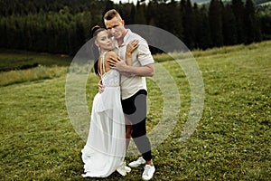 Beautiful fashionable couple at the park. Gorgeous woman in stylish white dress hugging handsome man , enjoy tenderness