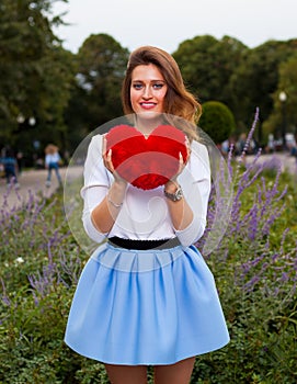 Beautiful fashionable Girl with red heart in the park in warm summer evening