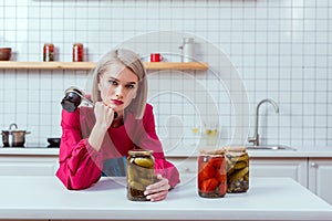 beautiful fashionable housewife looking at camera and holding seamer with jars of pickled vegetables