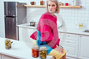 beautiful fashionable housewife sitting on kitchen counter with jars of pickled vegetables in
