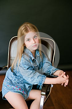 Beautiful fashionable little girl with blond hair in jeans clothes on a black background