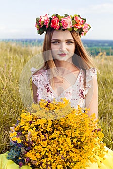 Beautiful fashionable pretty gorgeous girl in dress on the flowers field. Nice girl with wreath of flowers on her head and bouquet