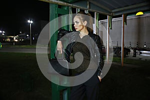 A beautiful fashionable red-haired girl poses at night on the street in the city, in autumn near a gas station