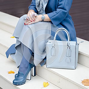 Beautiful fashionable shoes on women`s leg. Stylish ladies accessories. blue shoes and bag, coat with dress or skirt.