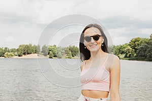 Beautiful fashionable woman outdoors. Young female model wearing sunglasses posing near lake.