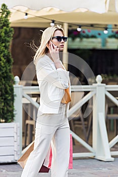 beautiful fashionable woman with shopping bags talking by smartphone and walking