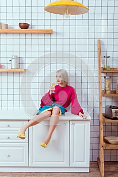 beautiful fashionable woman sitting on kitchen counter with cocktail glass and