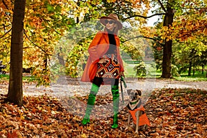 Beautiful fashionable Woman is wearing Fall clothes and is walking with dog in Autumn Scenery in park. Outdoor shoot. Autumn