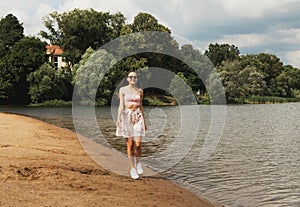 Beautiful fashionable woman. Young female model wearing sunglasses posing near lake.