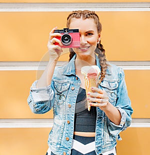 Beautiful fashionable young girl posing in a summer dress and denim jacket with pink vintage camera and multi-colored ice cream.