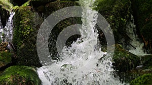 A beautiful fast clean live stream of a mountain stream falling on a slow motion stone. Drops of water are scattered