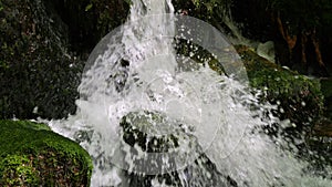 A beautiful fast clean live stream of a mountain stream falling on a slow motion stone. Drops of water are scattered