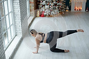 A beautiful fat woman in a sports uniform is exercising in the body to burn fat. Fitness and yoga. Sports at Christmas.