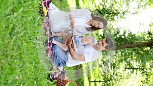 Beautiful father and mother read a book to their child, look at educational pictures, sitting in the park on a blanket