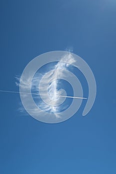 Beautiful feathery cloud with plane contrail piercing directly through